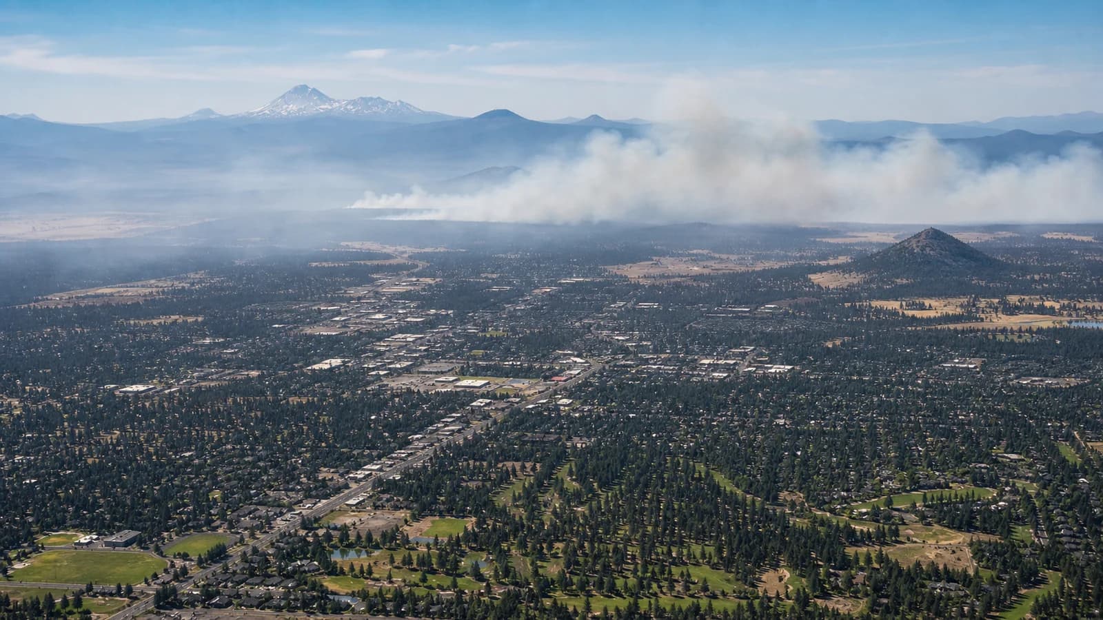 Aerial view of Central Oregon with wildfire smoke drifting unevenly across forest, town, and high desert terrain