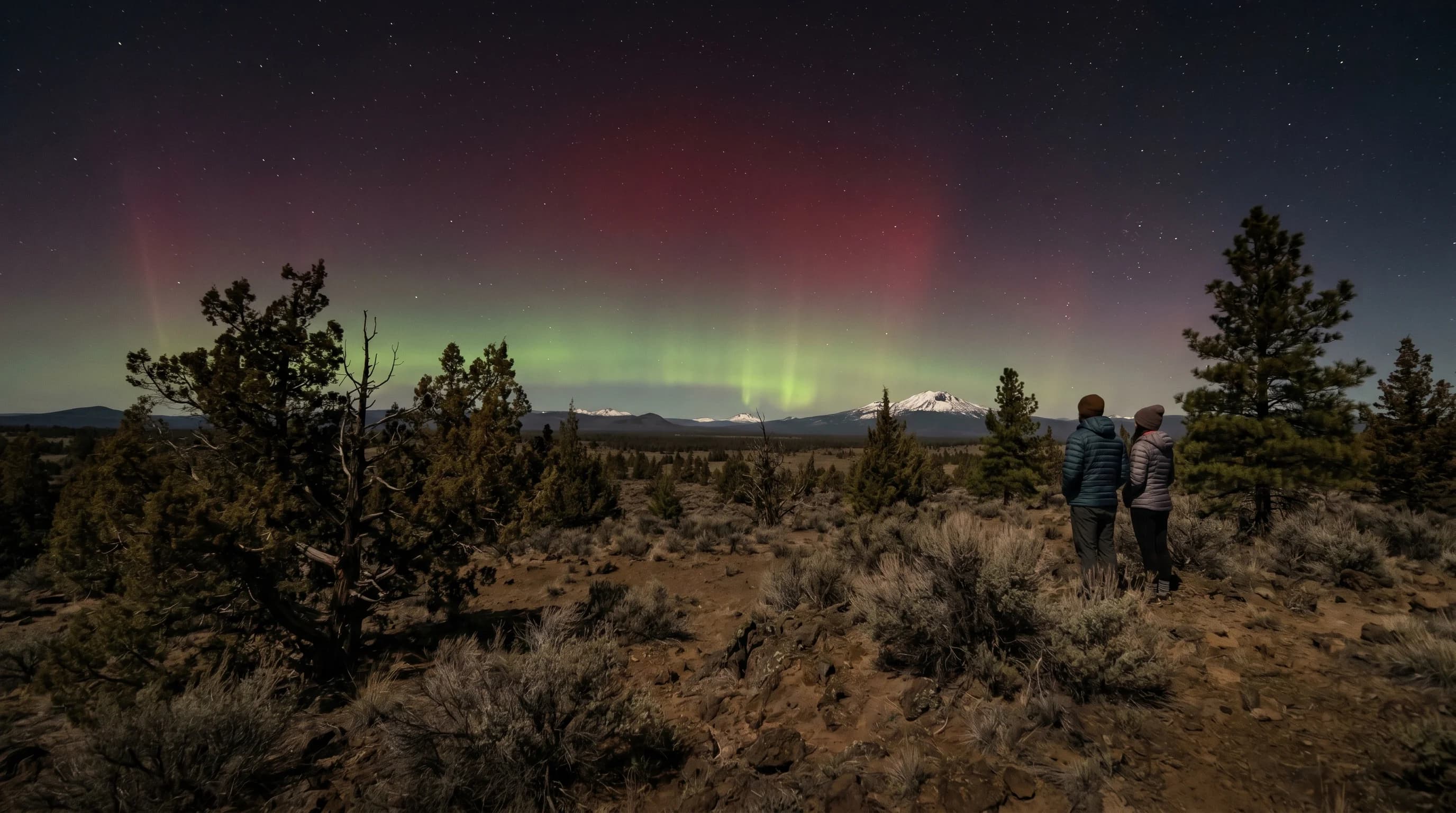 A faint green and red aurora glowing over the northern horizon above the high desert at night