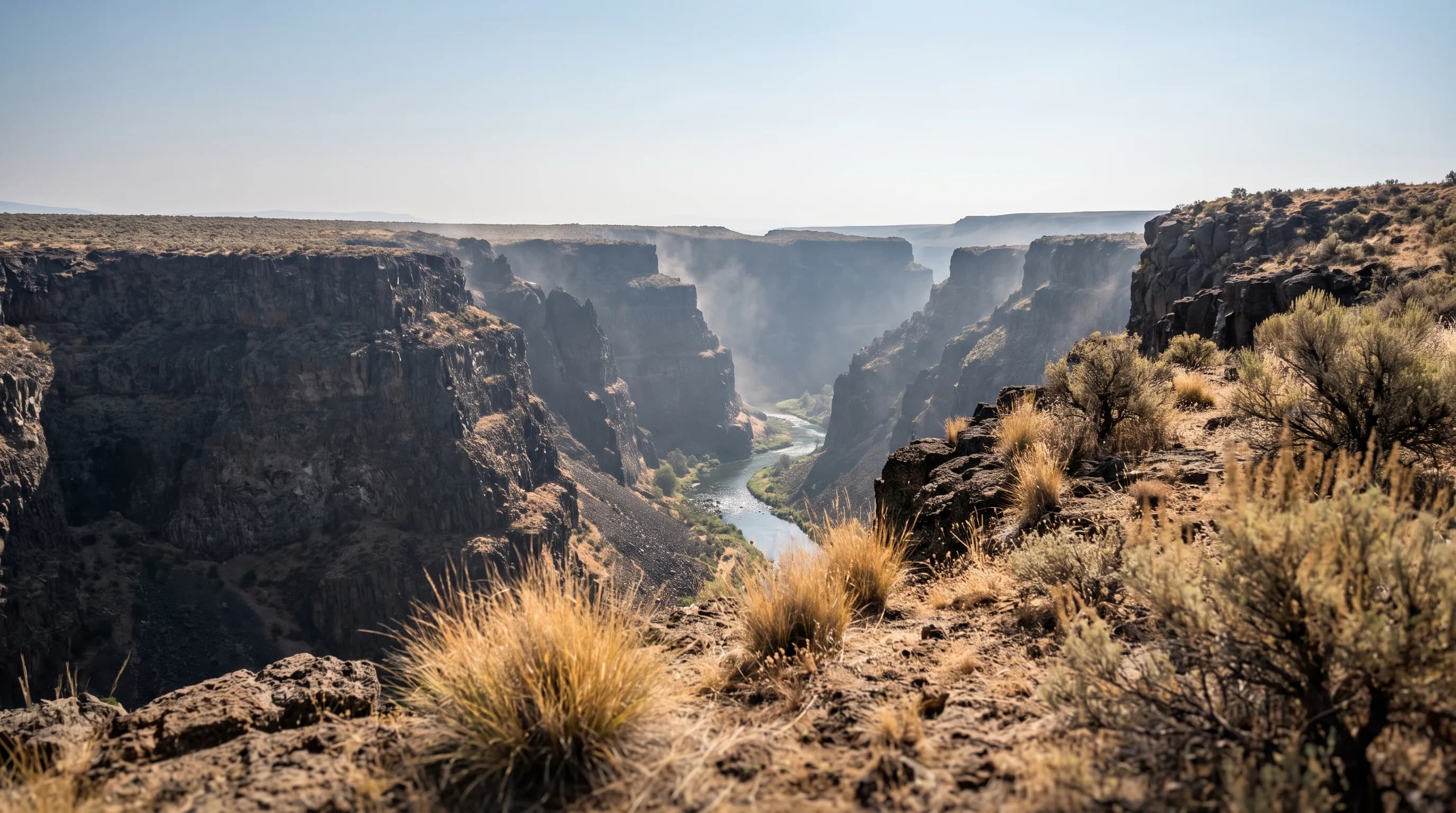Heat shimmer over dark basalt cliffs and dry grass above a river in a deep Central Oregon canyon