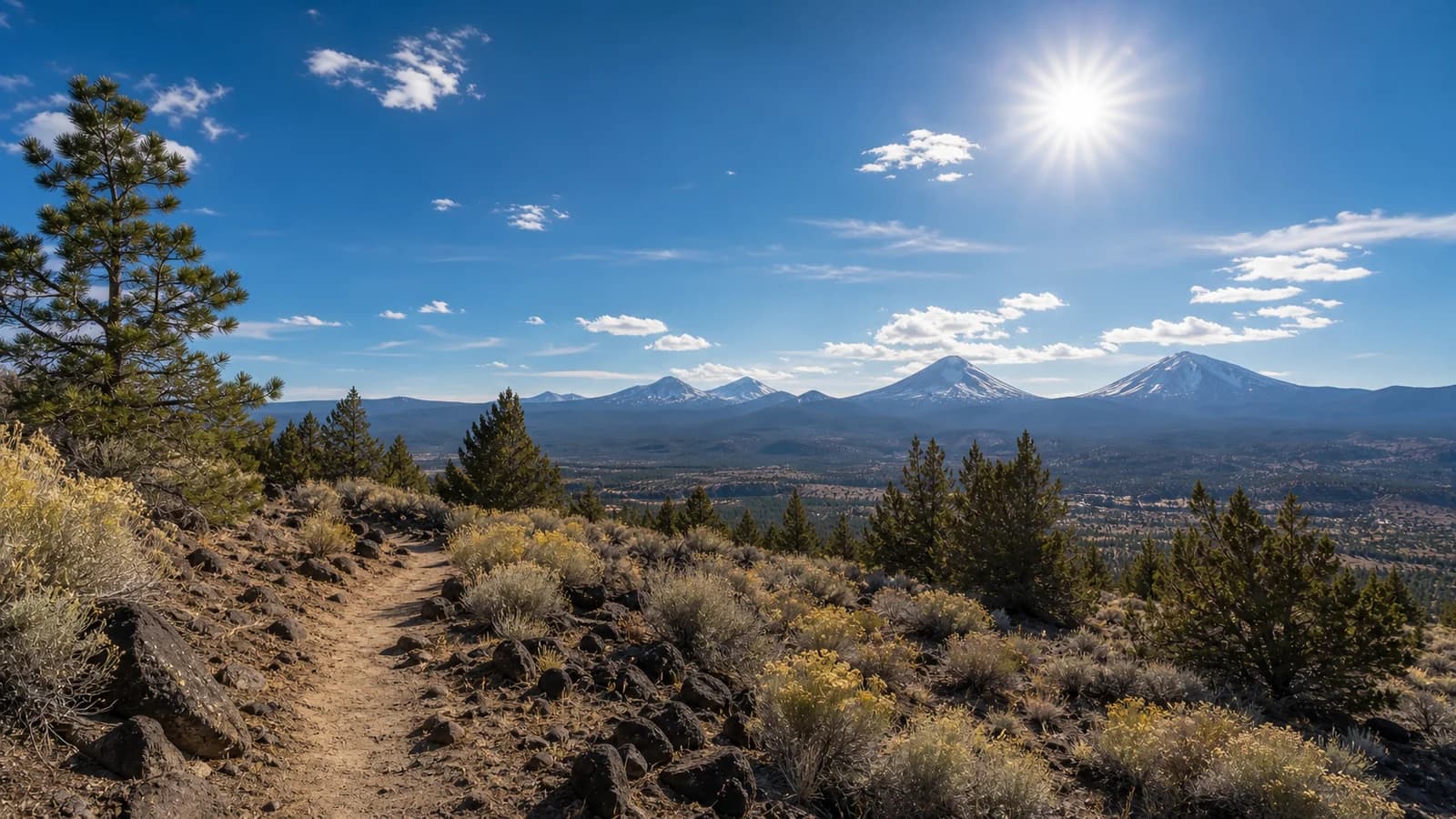 Bright Central Oregon trail under strong high desert sun with sagebrush, pines, and distant snowy Cascade peaks